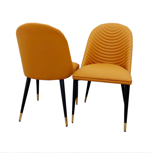 Set of two tan leather dining chairs with curved backs and black legs with gold tips