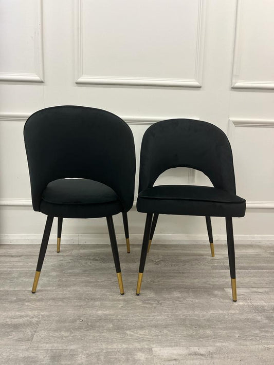 Set of two black velvet dining chairs with curved backs and gold-tipped legs
