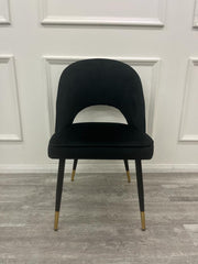 Black velvet dining chair with a cutout back and gold-tipped legs