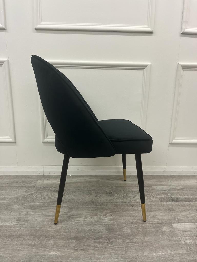 Side view of a black velvet dining chair with curved back and gold-tipped legs