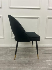 Side view of a black velvet dining chair with curved back and gold-tipped legs