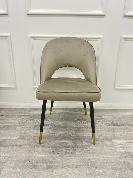 Champagne velvet dining chair with a rounded open-back design and black legs with gold tips