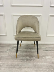 Champagne velvet dining chair with a rounded open-back design and black legs with gold tips