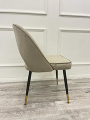 Side view of a champagne velvet dining chair with a curved back and black-and-gold legs
