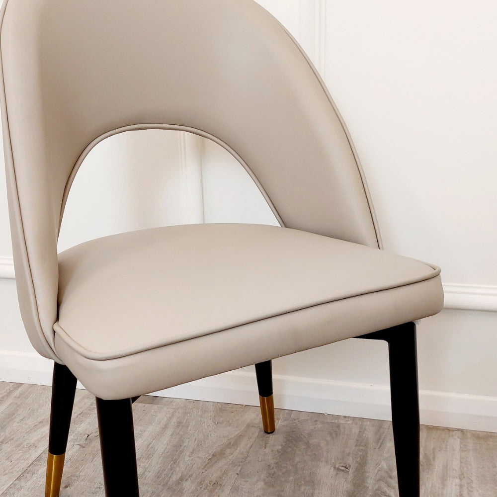Beige leather dining chair detail showing its curved back and piped seat cushion