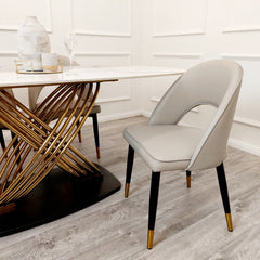 Beige leather dining chair with a curved open-back design and black legs with gold-tone tips