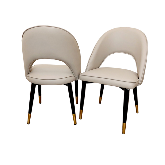 Set of two beige leather dining chairs with curved backs and black legs with gold-tone tips