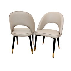 Set of two beige leather dining chairs with curved backs and black legs with gold-tone tips