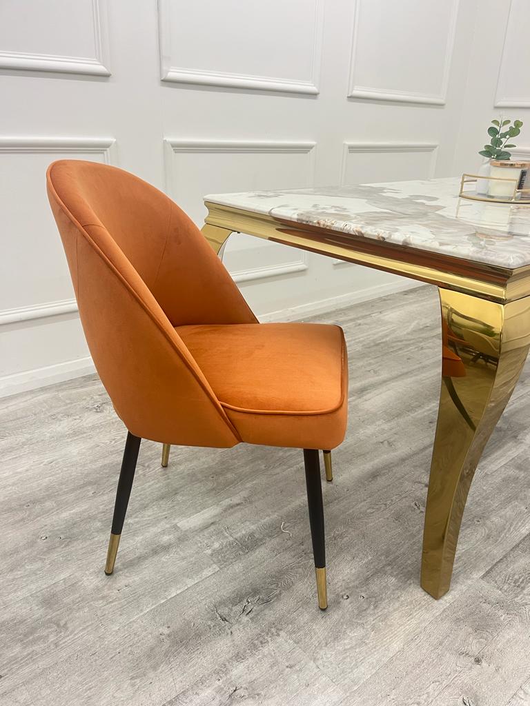 Side view of a rust velvet dining chair with curved back and tapered legs