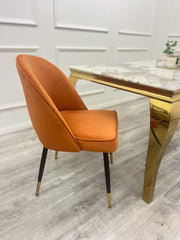 Side view of a rust velvet dining chair with curved back and tapered legs