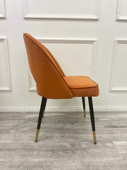 Side profile of rust velvet dining chair with a curved back and tapered legs