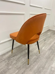 Rear view of rust velvet dining chair with curved upholstered back and black, gold-tipped legs