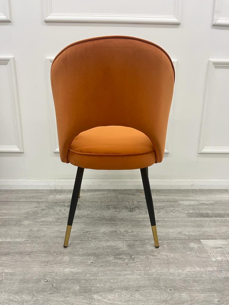Front view of rust velvet chair with rounded back and black, gold-tipped legs