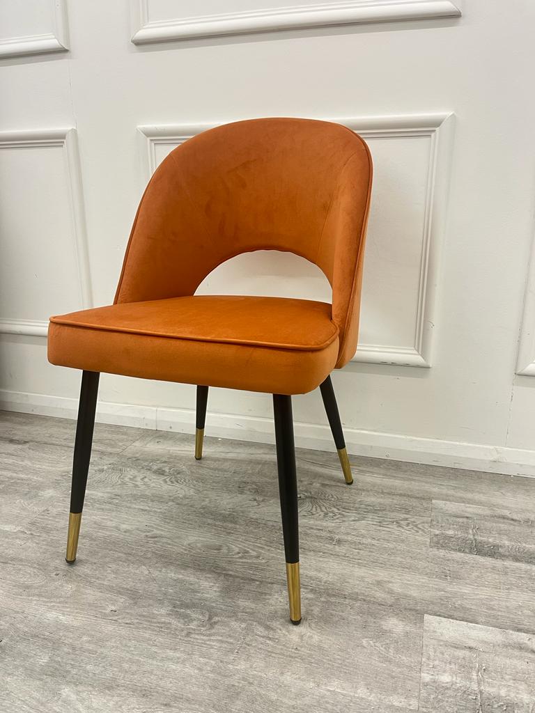 Angled view of rust velvet chair with arched back cutout and tapered legs