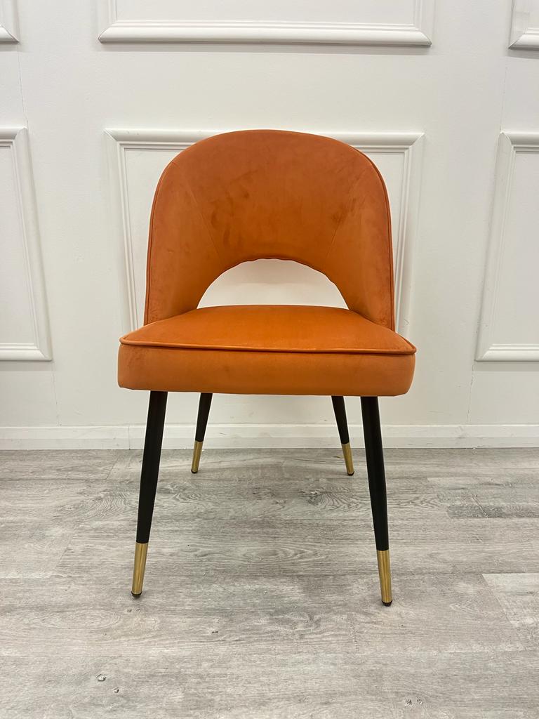 Rust velvet dining chair with a cutout below the curved back and tapered legs