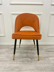 Rust velvet dining chair with a cutout below the curved back and tapered legs