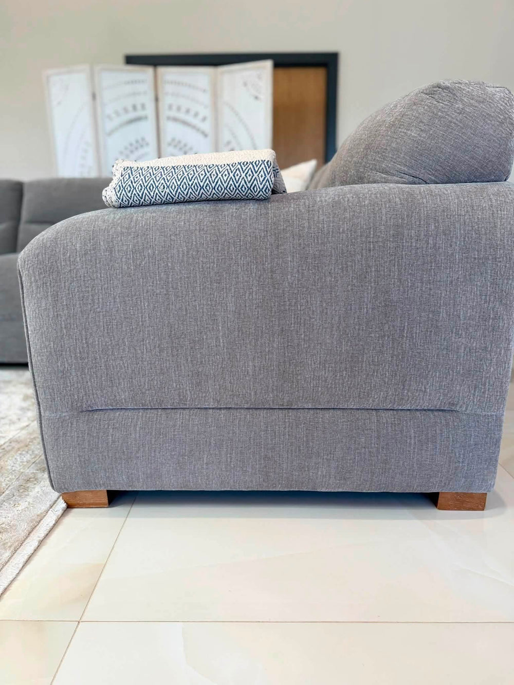 Close view of the gray sofa's upholstered side panel and wooden feet