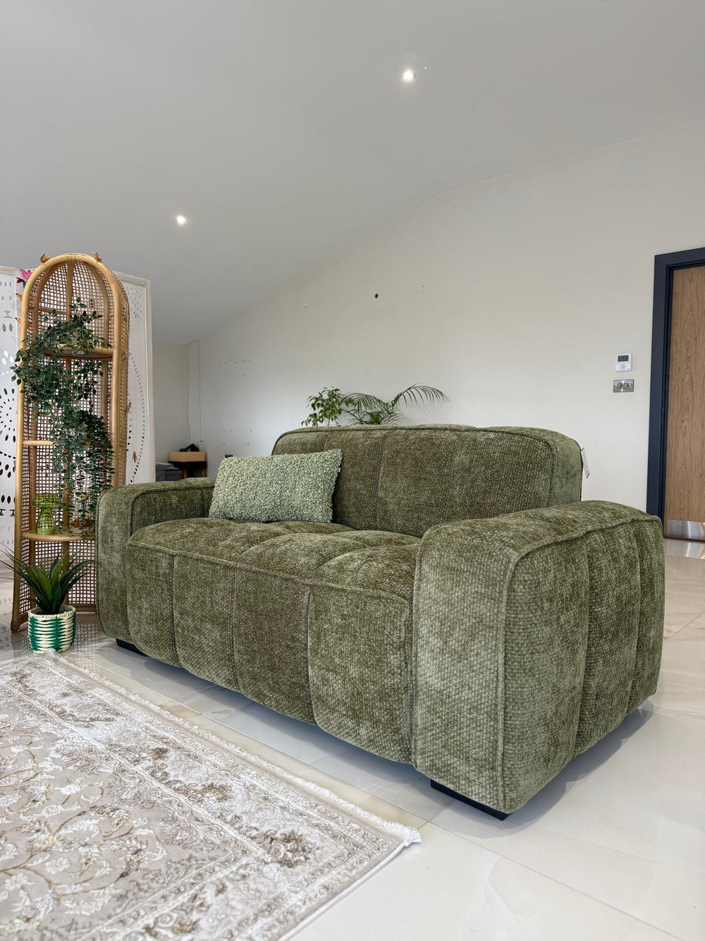 Olive green two-seater sofa with thick padded arms, deep seats, and a matching textured pillow.