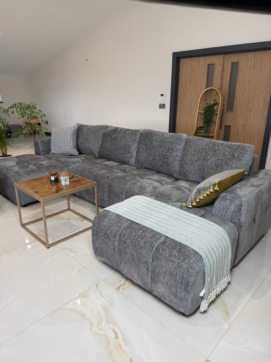 Gray U-shaped sofa bed arranged with cushions and a throw blanket