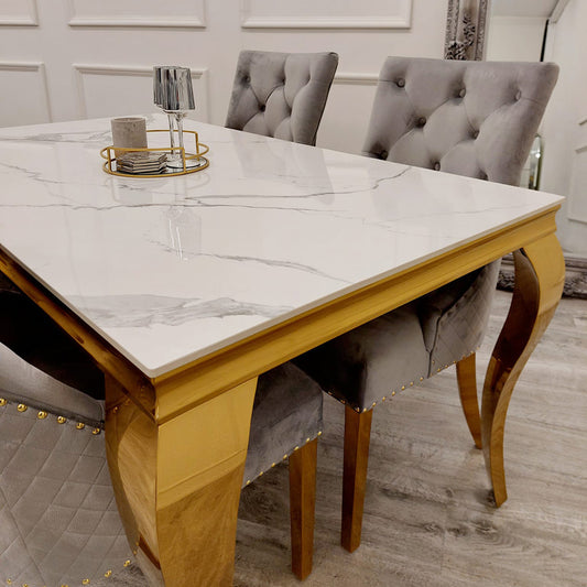 Dining table with a veined white top and sculpted gold legs, shown with gray chairs