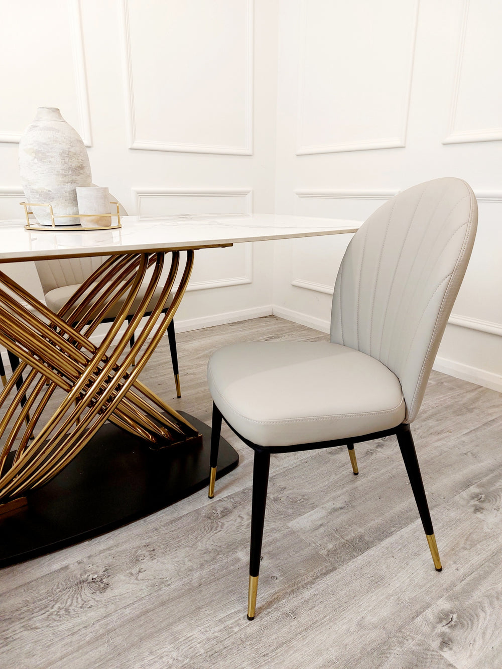 Dining table's veined white top and intertwined gold base beside a beige chair