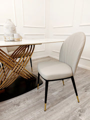 Dining table's veined white top and intertwined gold base beside a beige chair