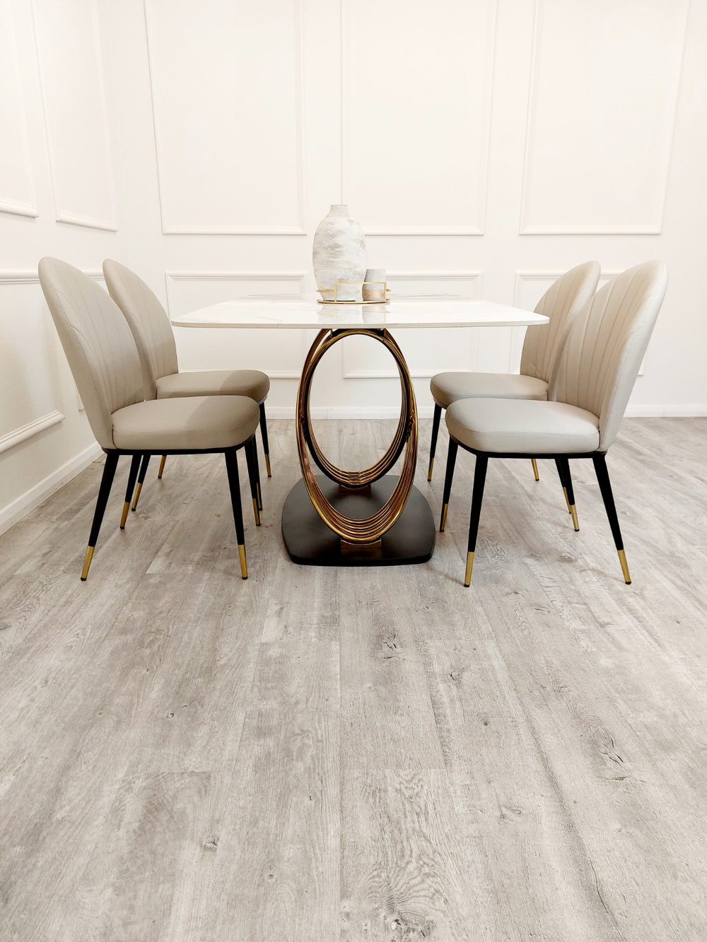Dining table with oval gold pedestal detail, shown between four beige chairs