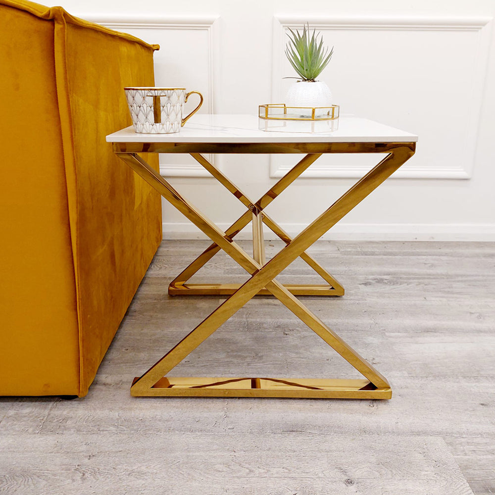 Lamp table with white top and geometric gold base beside a sofa
