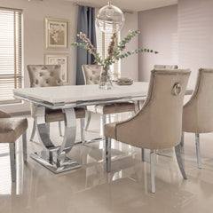 Arriana dining table with a pale stone top and curved metal supports, surrounded by chairs
