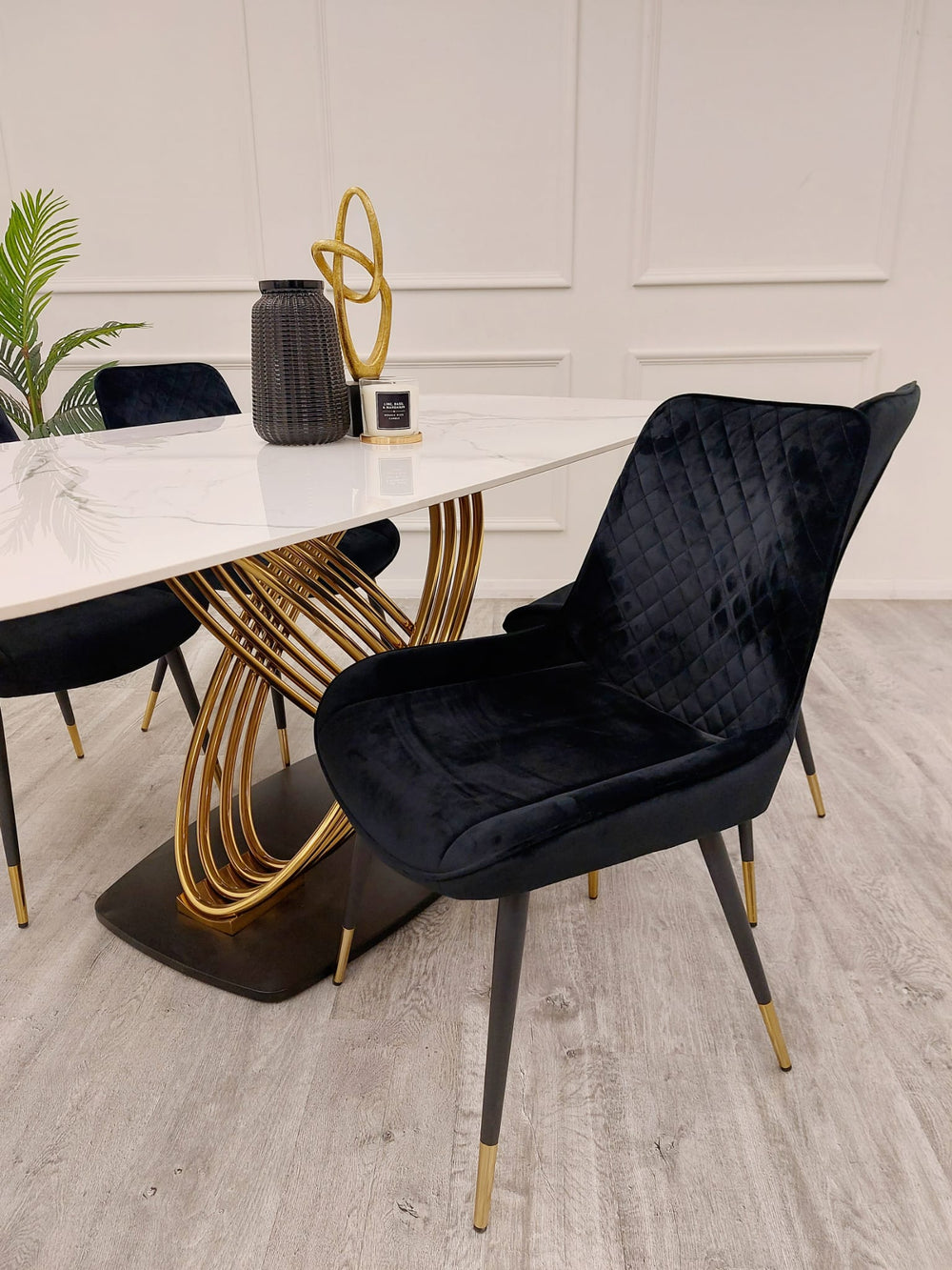 White stone dining table with sculptural gold base, paired with black chairs