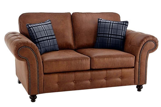 Two-seat brown sofa with rolled arms, nailhead trim, buttoned front, and two plaid cushions