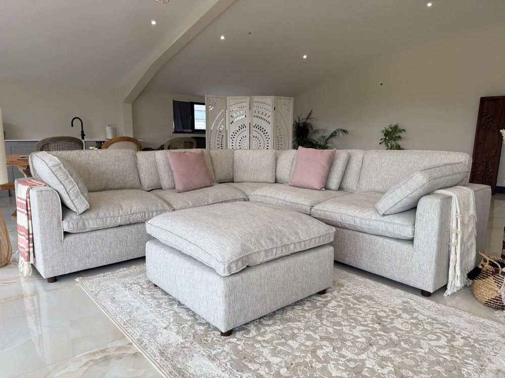 Large light gray corner sofa with matching footstool and loose cushions