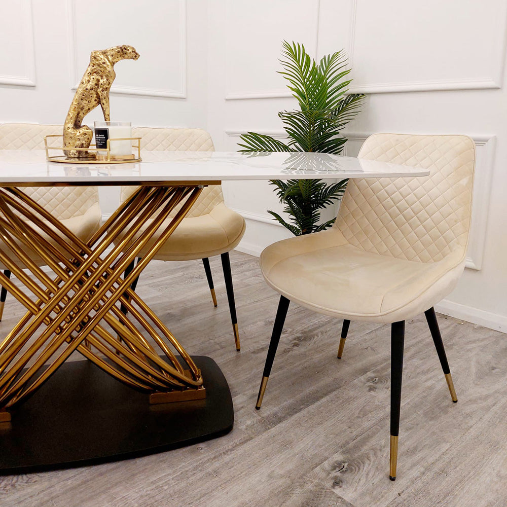 White stone-top dining table with curved gold-tone base, shown beside cream chairs